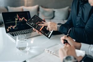 Professionals analyzing financial data on a tablet and laptop in an office setting.